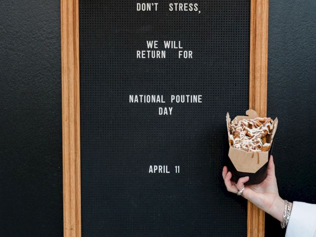 A sign reads "Don't stress, we will return for National Poutine Day April 11," with a hand holding poutine.