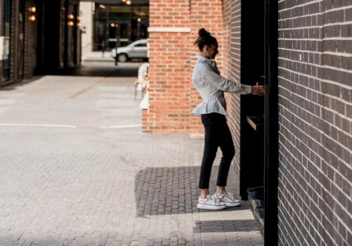 A person is using an ATM on a street with brick walls and cobblestone pavement, under city lights in the background.