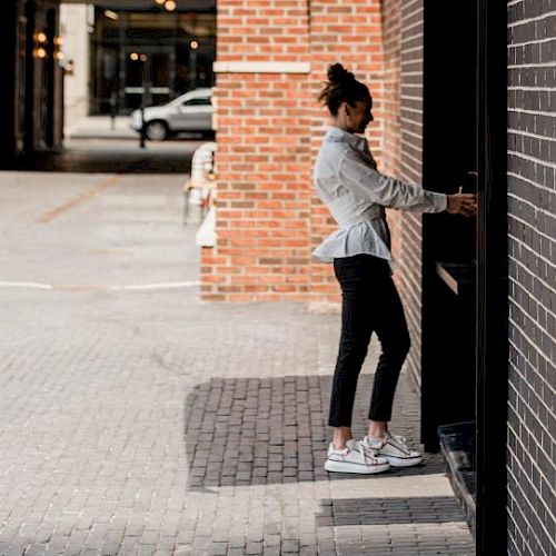 A person is using an ATM on a street with brick walls and cobblestone pavement, under city lights in the background.