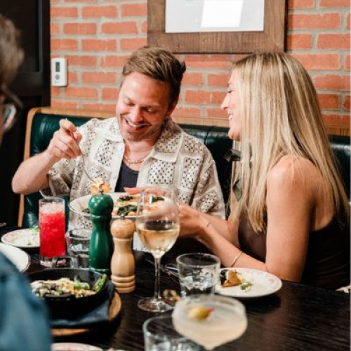 A group of people enjoying a meal at a restaurant, with drinks and food on the table, engaging in conversation and laughter.
