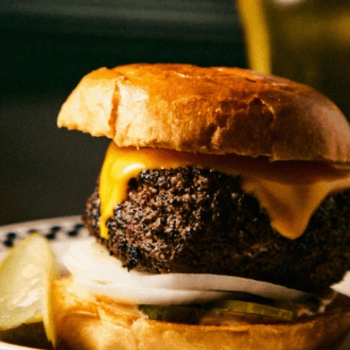 A cheeseburger with a beef patty, melted cheese, onions, and pickles on a bun, served with a side of pickle slices.