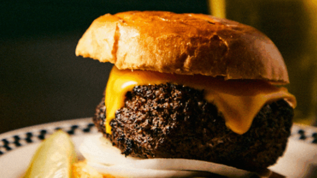 A cheeseburger with a beef patty, melted cheese, onions, and pickles on a bun, served with a side of pickle slices.