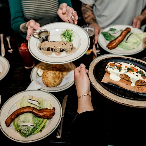 An overhead view of a table with various dishes, including salads, a burger, and platters, being shared among people.