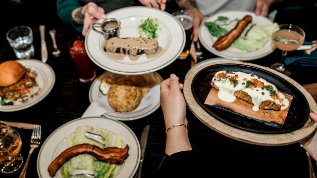 An overhead view of a table with various dishes, including salads, a burger, and platters, being shared among people.