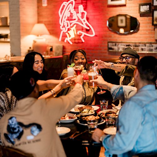 A group of people is toasting with drinks around a table in a cozy restaurant with a warm, inviting atmosphere.
