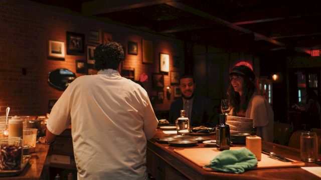 A cozy dimly lit bar or cafe with people chatting at a long wooden counter, warm lights, and drinks on the table, intimate evening vibe.