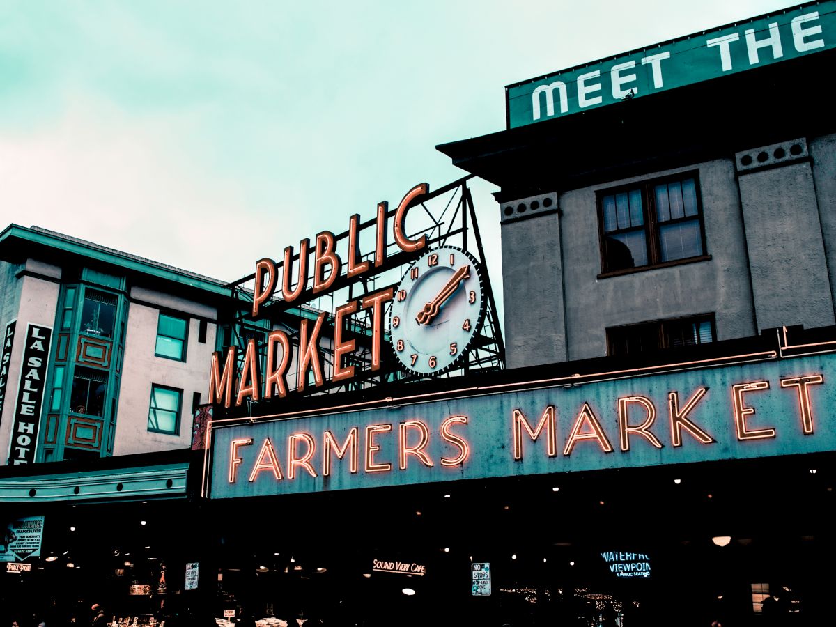The image shows the neon signs of a public market and farmers market with a clock in an urban setting, capturing a classic market vibe.